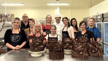 Kids happily engaged in a cooking class in Perth. They are gathered around a spacious countertop, wearing aprons and chef hats.