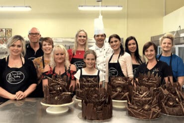 Kids happily engaged in a cooking class in Perth. They are gathered around a spacious countertop, wearing aprons and chef hats.